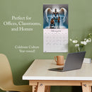 Calendar on a wall above a desk with a laptop and mug, against a green wall.