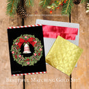 Christmas card with wreath design, red envelope, and gold foil card on wooden surface