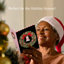 Woman wearing a Santa hat holding a Christmas card with a wreath design, surrounded by holiday decorations.