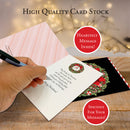 Hand holding a Christmas card with wreath design on a wooden surface, surrounded by other cards.